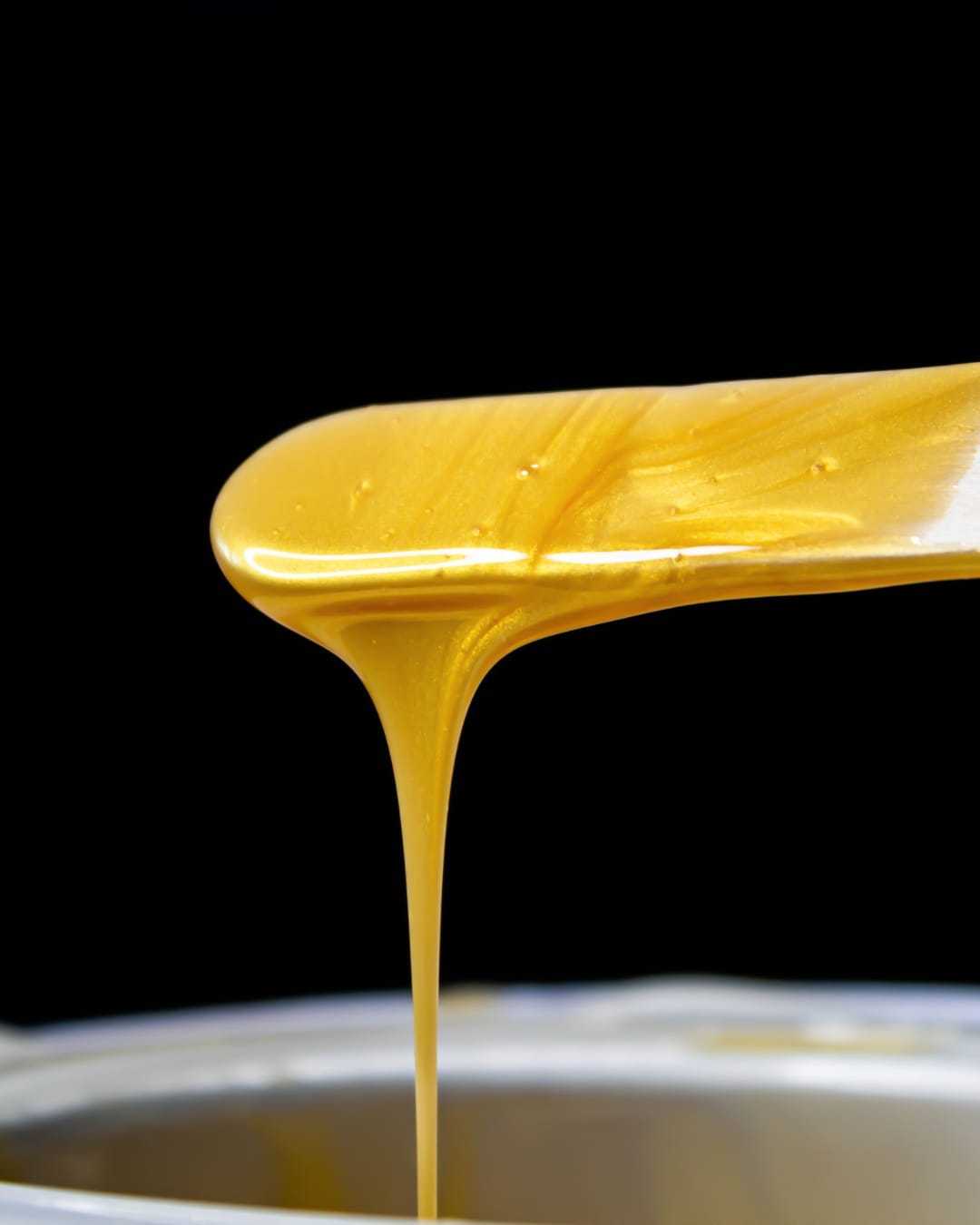 Golden honey flowing from a spatula against a black background.