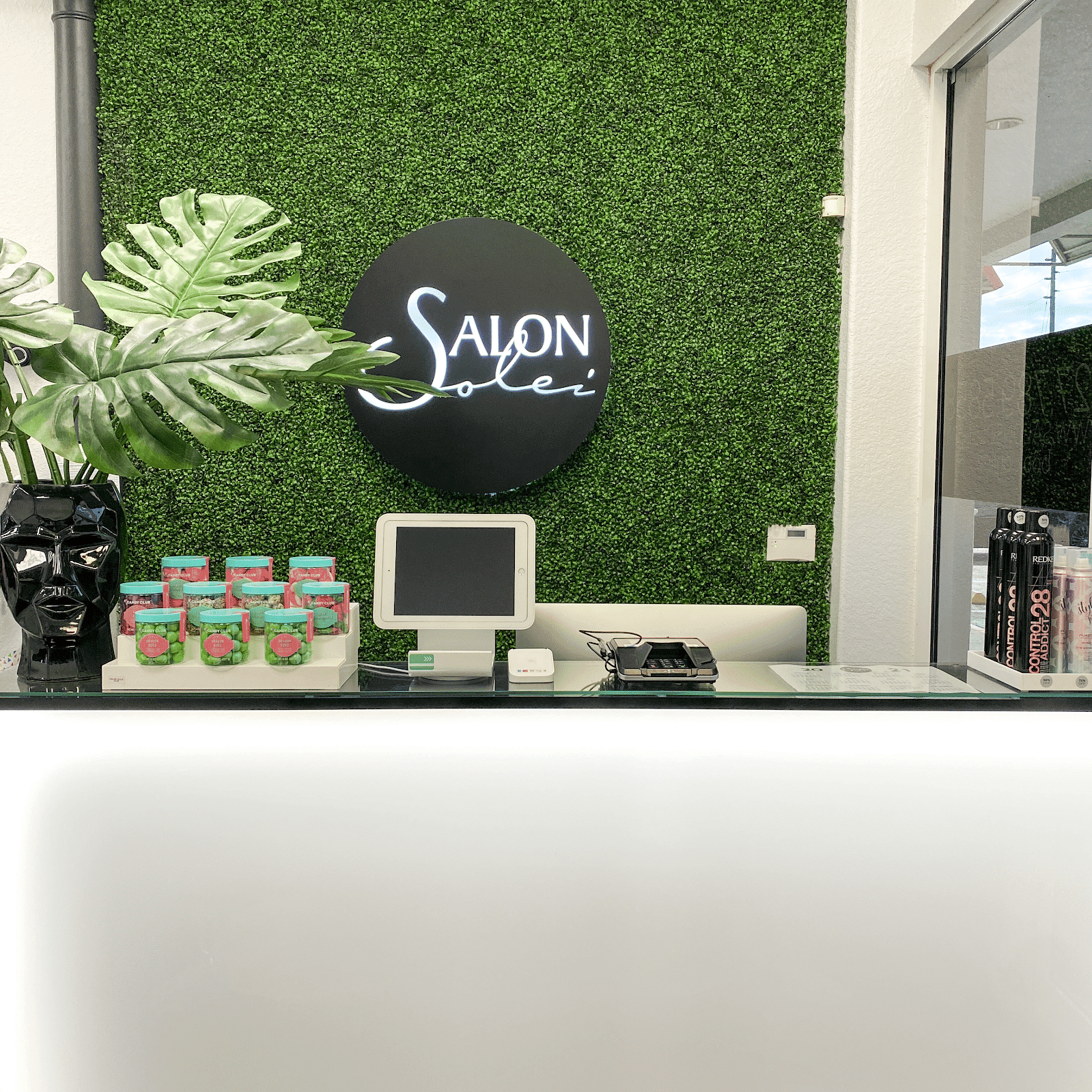 Reception desk at Salon Soleil with greenery wall and decor.