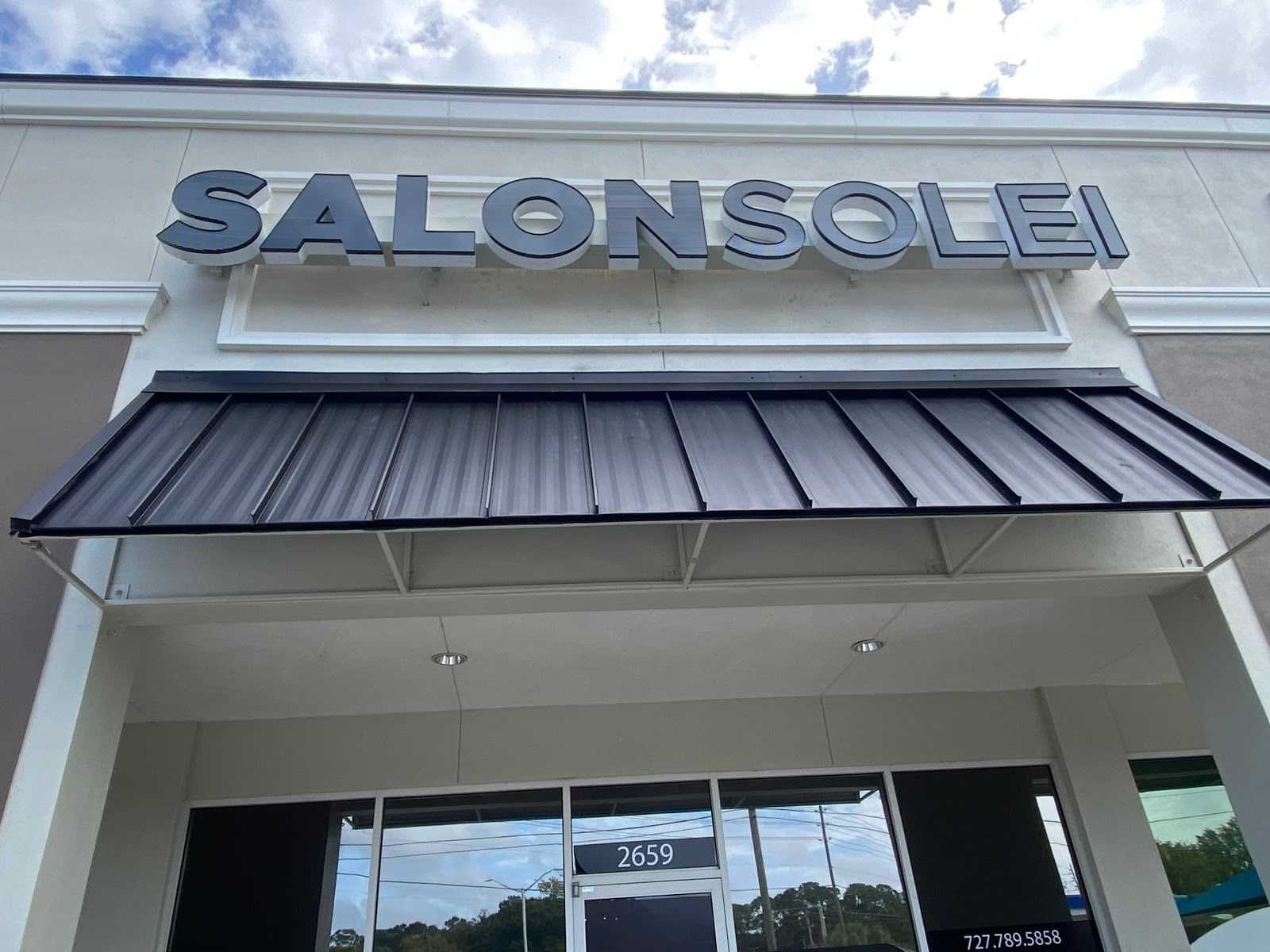 Exterior view of Salon Solei building with glass entrance and street reflections.