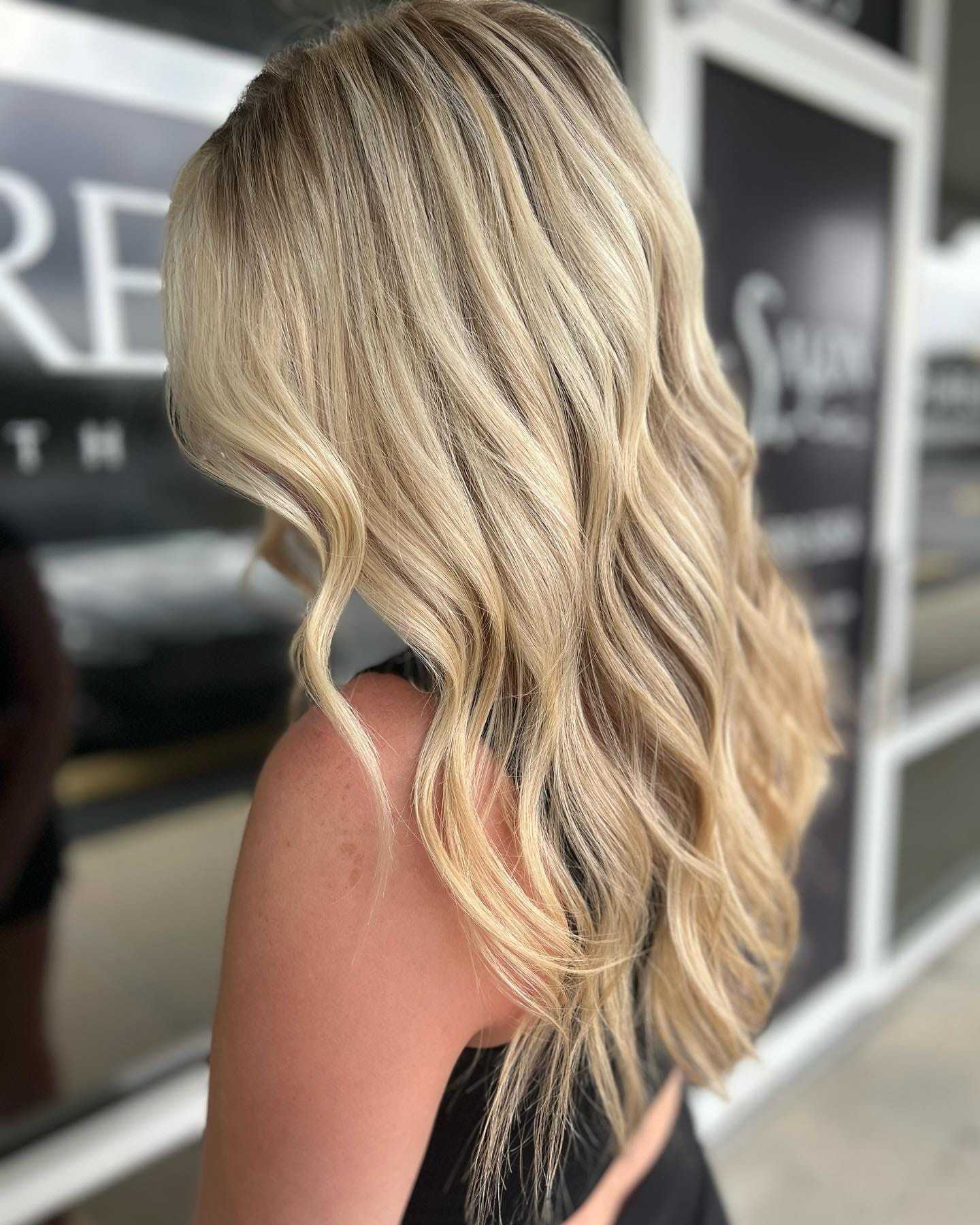 Blonde-haired woman with loose waves, facing away, in front of a salon window.